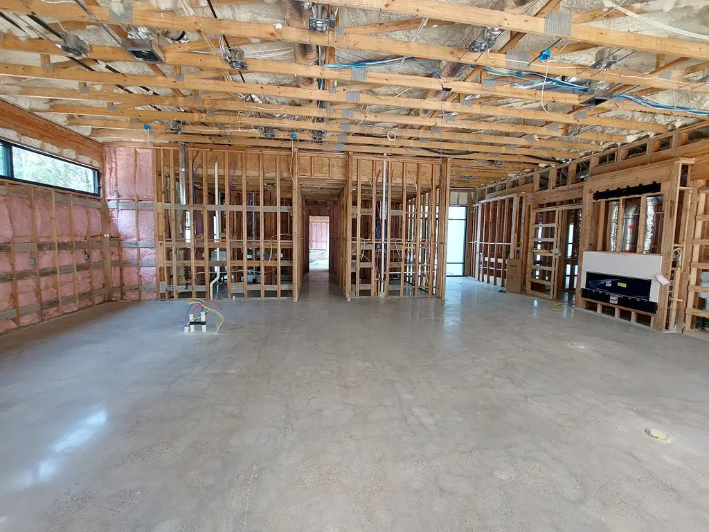 Bare concrete slab running through a house still in timber framing, already ground flat and reflecting the open joists overhead