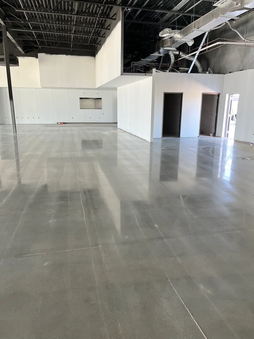 Mirror finish polished concrete floor in a white commercial fit out, reflecting the walls and ductwork above