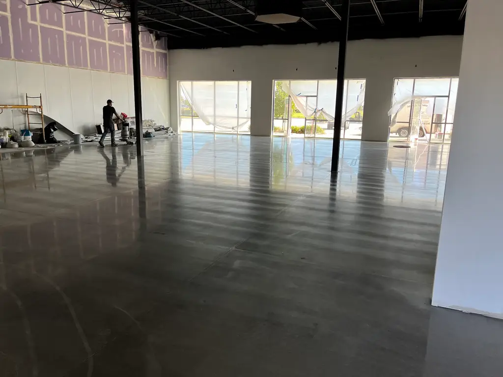 A Mimcon crew member walking a burnisher across a large polished concrete floor, with the company's branded van parked outside the storefront glazing behind him